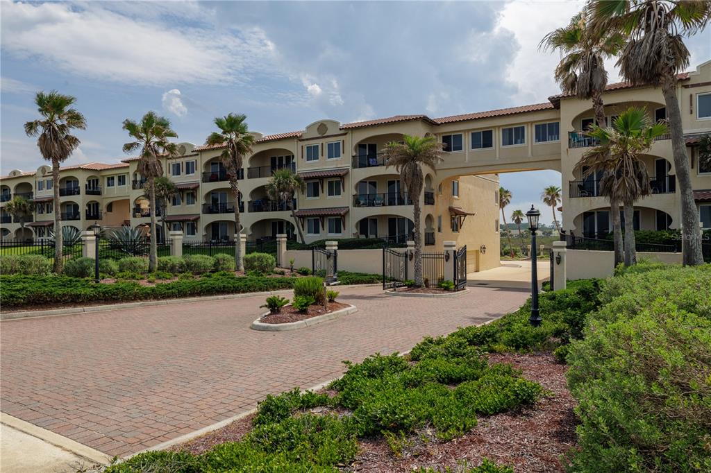 A multi-story Mediterranean-style apartment building features arched balconies, a paved driveway, and palm trees — 2450 N OCEAN SHORE BOULEVARD UNIT 313C, FLAGLER BEACH, FL