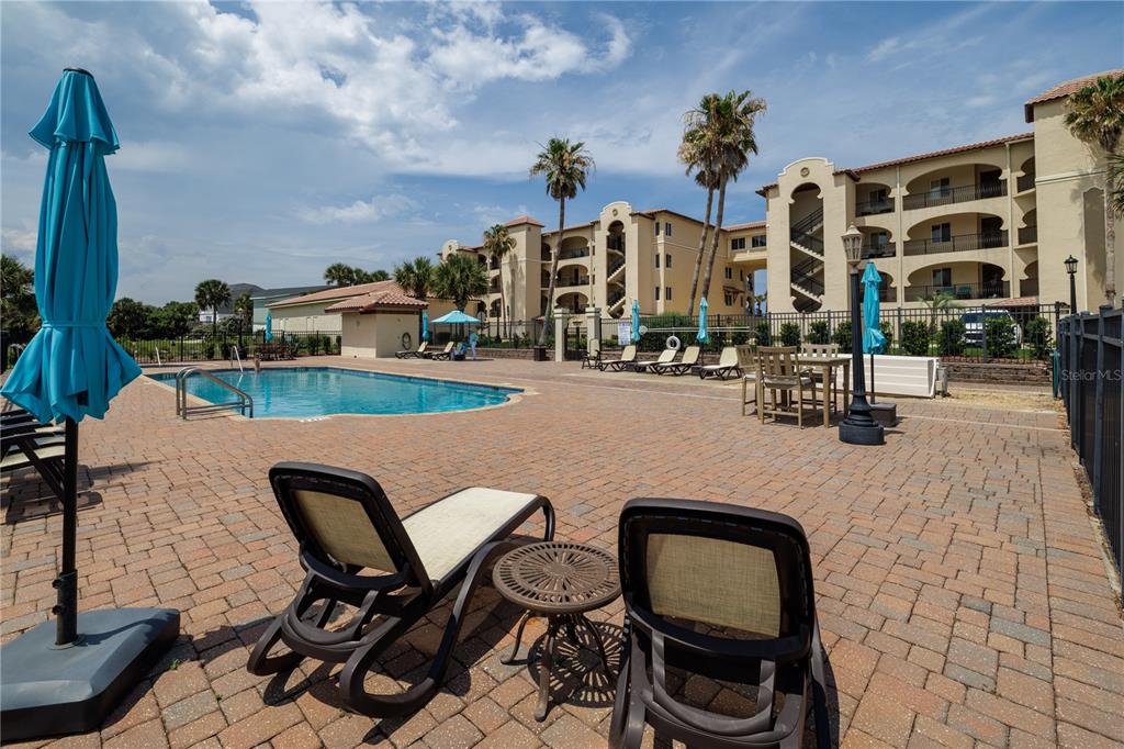 A swimming pool area with lounge chairs, tables, and a multi-story building in the background — 2450 N OCEAN SHORE BOULEVARD UNIT 313C, FLAGLER BEACH, FL