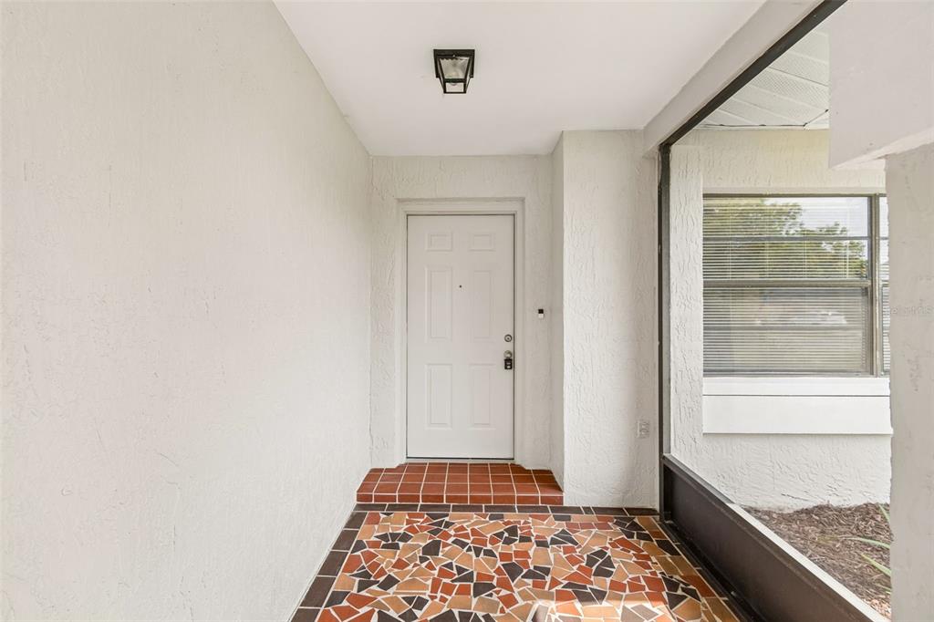 A covered entryway features a white front door, a mosaic tile floor, and a screen enclosure — 8526 HUNTSMAN LANE, PORT RICHEY, FL