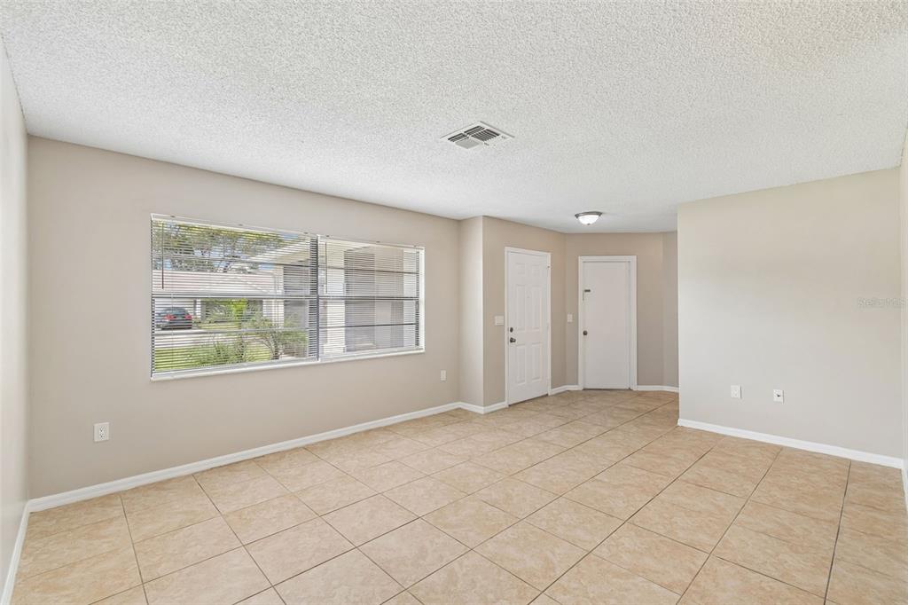 An empty room with beige tile flooring, white walls, a large window, and two doors — 8526 HUNTSMAN LANE, PORT RICHEY, FL