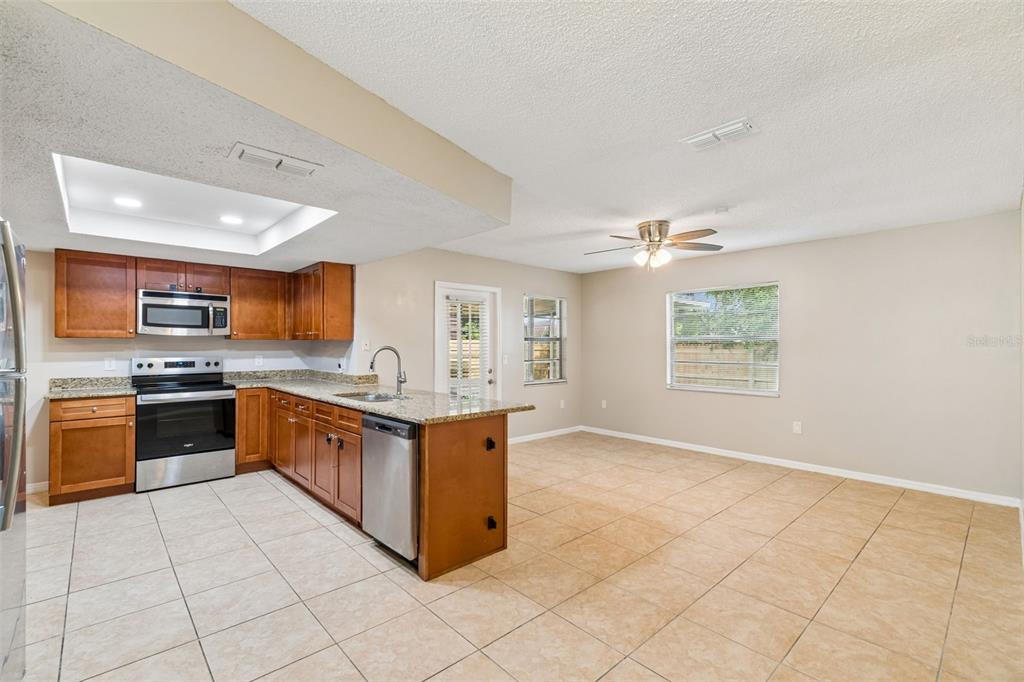A kitchen with wood cabinets, granite countertops, and stainless steel appliances opens to a dining area — 8526 HUNTSMAN LANE, PORT RICHEY, FL