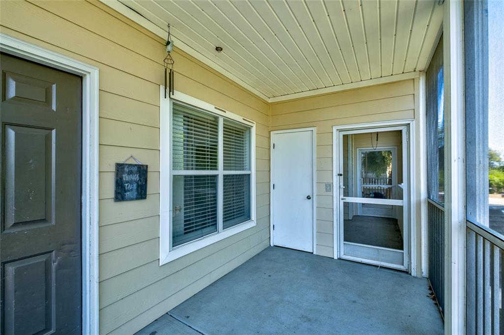 A covered outdoor patio with beige siding, a window, and a screened-in entry door — 4802 51ST STREET W UNIT 1015, BRADENTON, FL
