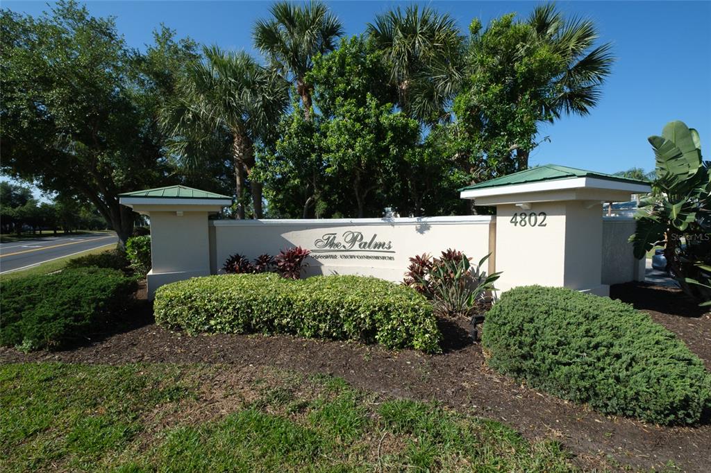 A beige monument sign for The Palms condominiums stands in front of lush landscaping and trees — 4802 51ST STREET W UNIT 1015, BRADENTON, FL