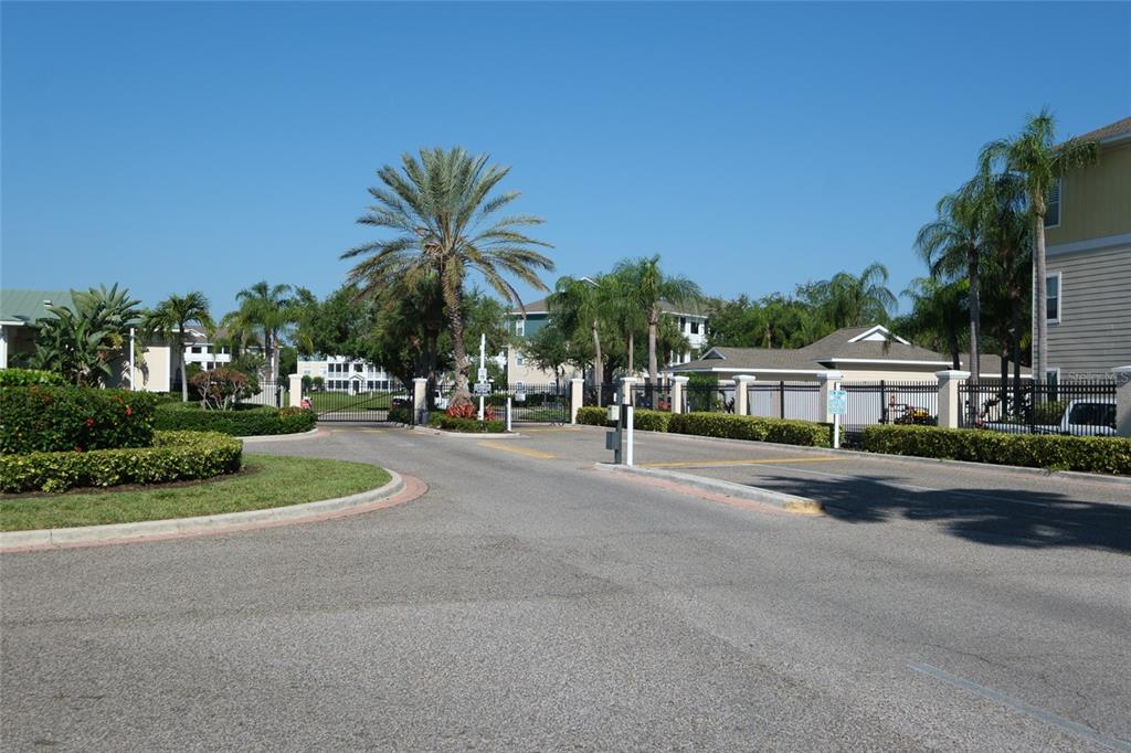 A gated entrance with a paved road, palm trees, and surrounding residential buildings — 4802 51ST STREET W UNIT 1015, BRADENTON, FL