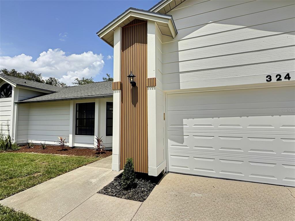The exterior of a house features white horizontal siding, a garage, and wood-slat accent detailing — 324 RINGWOOD CIRCLE, WINTER SPRINGS, FL