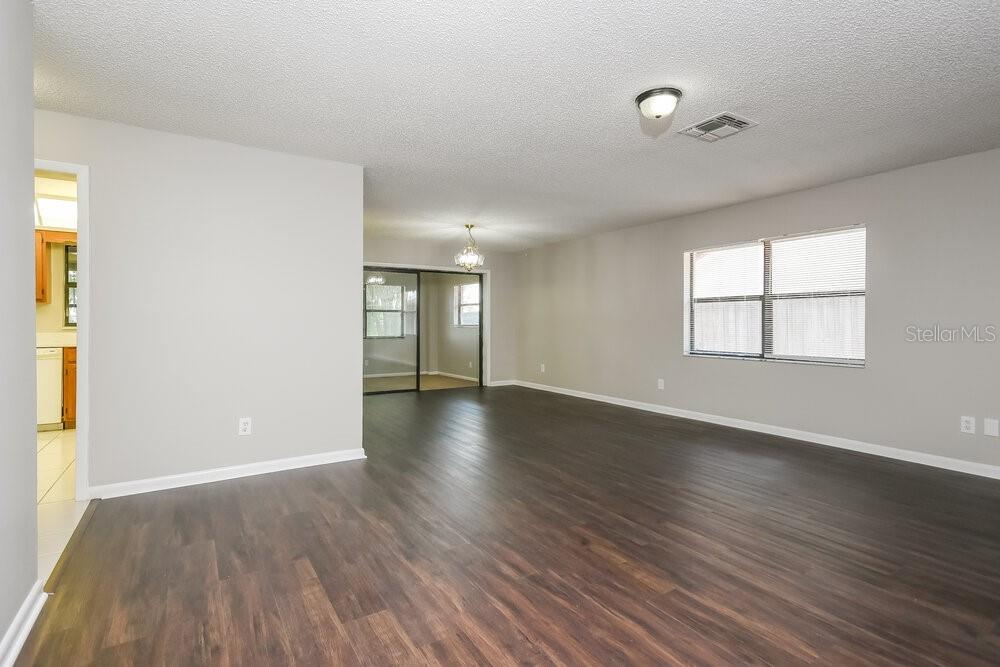 An empty living room features dark wood-look flooring, light gray walls, and a large window — 104 LAKE DAISY TERRACE, WINTER HAVEN, FL