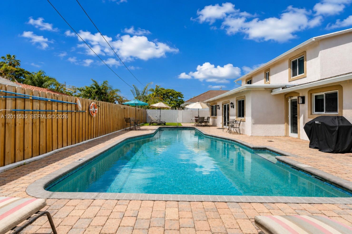 A backyard swimming pool sits on a paved patio next to a two-story house — 1660 NE 25th Ave, Pompano Beach FL 33062, POMPANO BEACH, FL