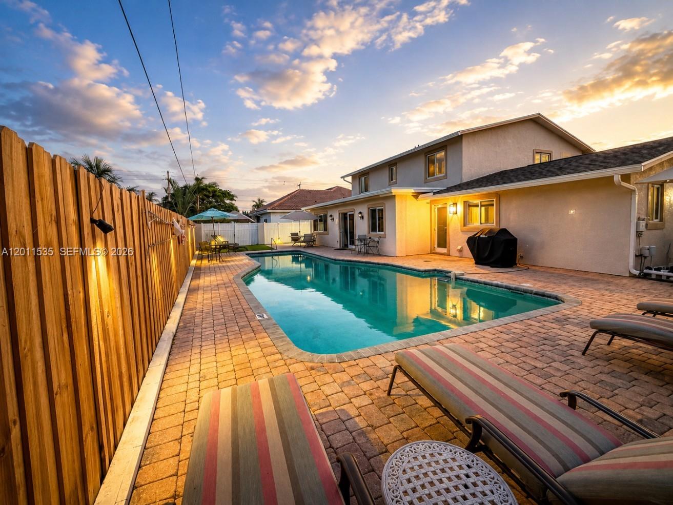A backyard features a swimming pool, brick patio, lounge chairs, and a wooden privacy fence — 1660 NE 25th Ave, Pompano Beach FL 33062, POMPANO BEACH, FL