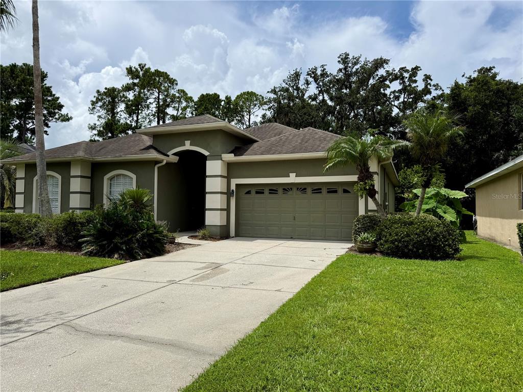 A single-story house with a green exterior, a two-car garage, and a concrete driveway — 5126 MAJESTIC WOODS PL, SANFORD, FL