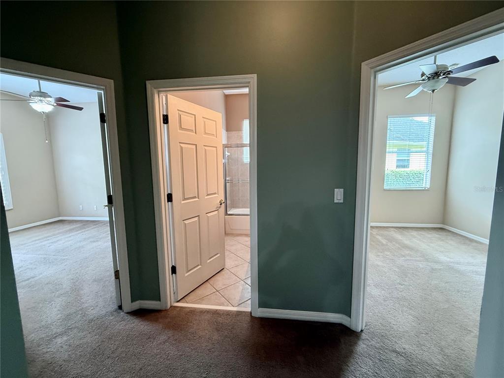 A hallway with green walls leads to two carpeted bedrooms and a central tiled bathroom — 5126 MAJESTIC WOODS PL, SANFORD, FL