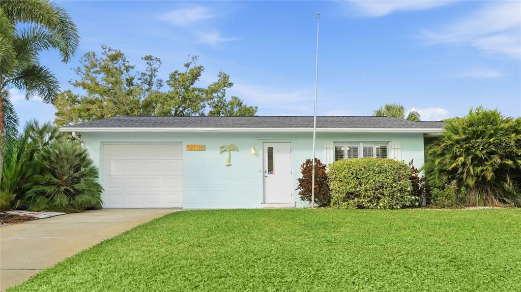 A light blue single-story house features a white garage door, front door, and green lawn — 2165 LAKEWOOD DRIVE, NOKOMIS, FL