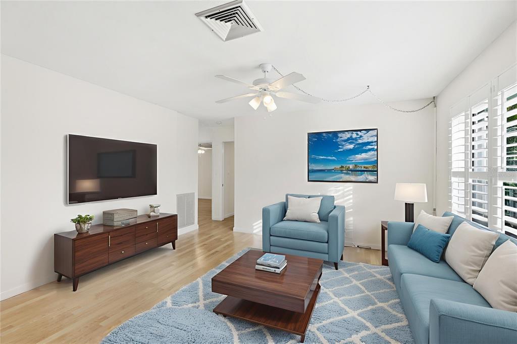 A living room features light wood floors, blue furniture, a television, and a ceiling fan — 2165 LAKEWOOD DRIVE, NOKOMIS, FL