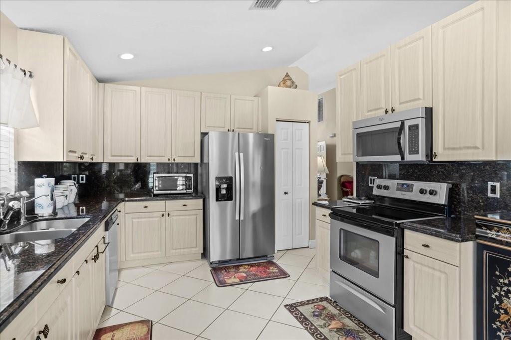 A kitchen features light-colored cabinets, dark granite countertops, stainless steel appliances, and tiled flooring — 6358 Westchester Club Drive, Boynton Beach FL 33437, BOYNTON BEACH, FL