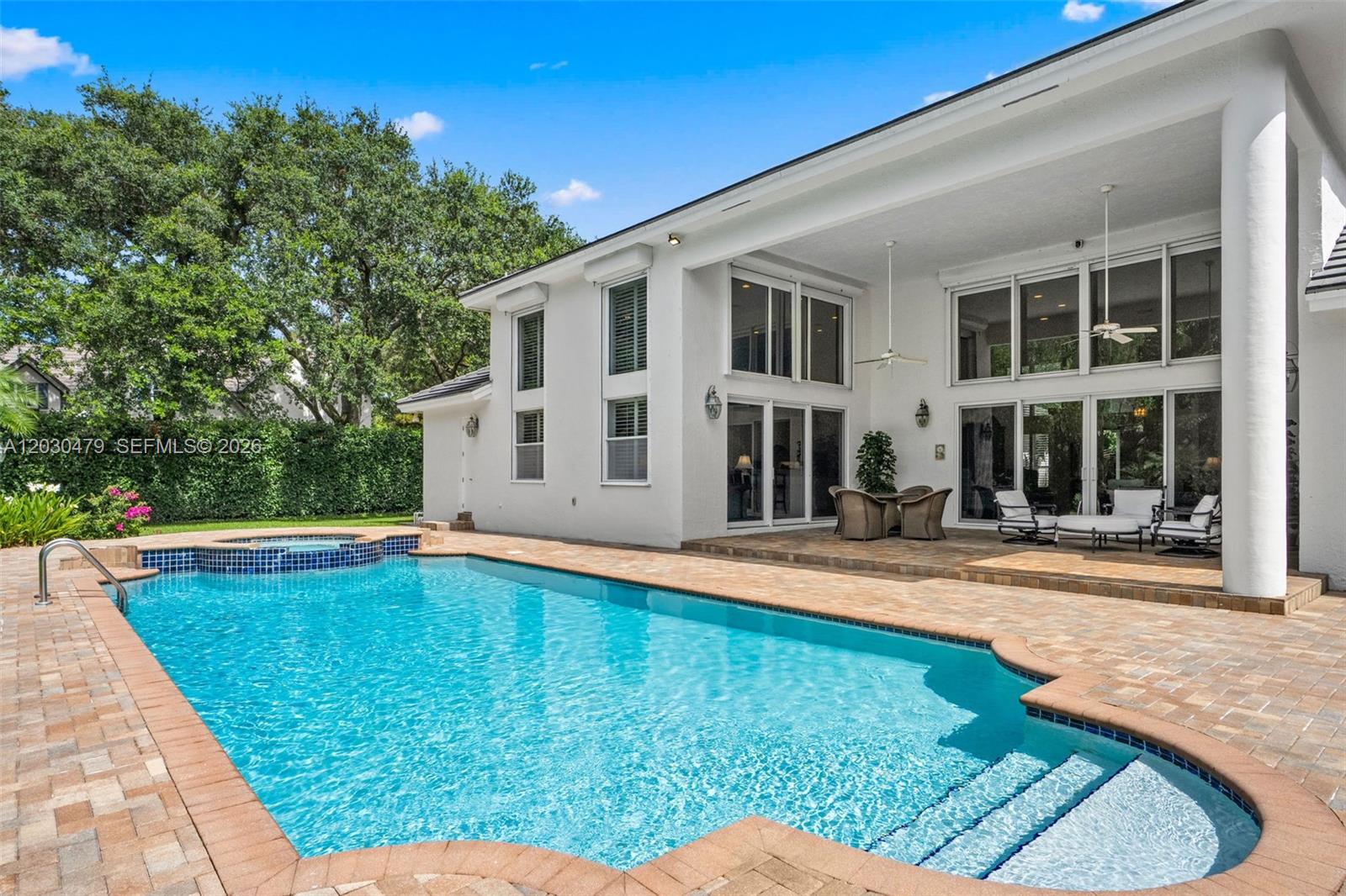A white two-story house features a large swimming pool with a spa on a patio — 6020 W Suburban Dr, Pinecrest FL 33156, PINECREST, FL