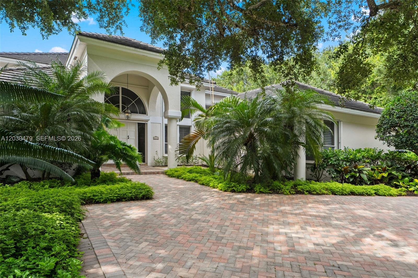 A white house with a large arched entryway and a brick paver driveway — 6020 W Suburban Dr, Pinecrest FL 33156, PINECREST, FL