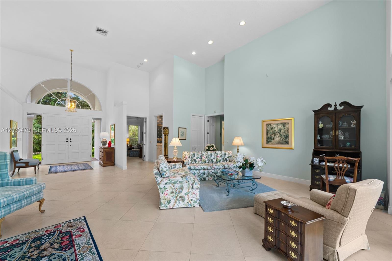 A spacious living room features high ceilings, light tile floors, and floral-patterned furniture — 6020 W Suburban Dr, Pinecrest FL 33156, PINECREST, FL
