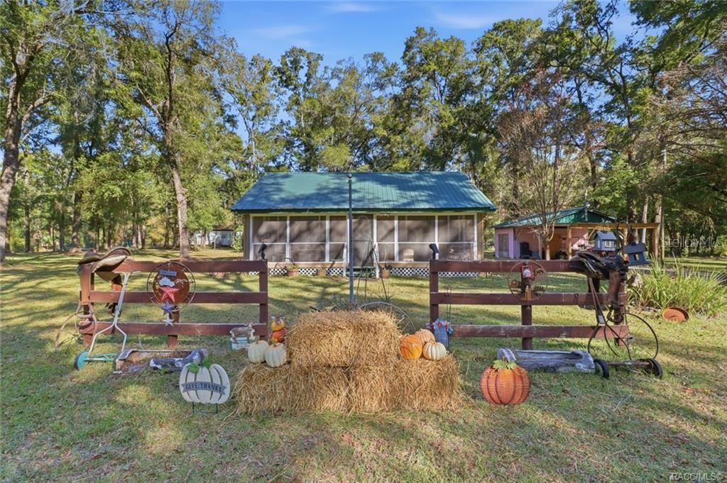 A rustic wooden fence decorated with hay bales and pumpkins stands before a screened-in cabin — 8110 SW 88TH LANE, TRENTON, FL