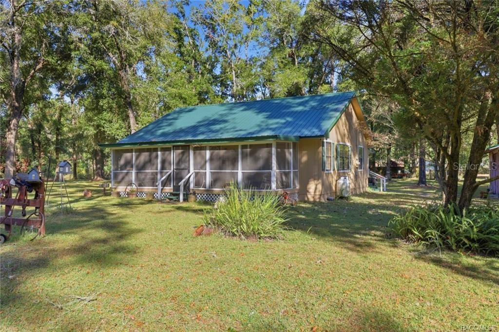 A single-story house with a green metal roof and a large screened-in front porch — 8110 SW 88TH LANE, TRENTON, FL