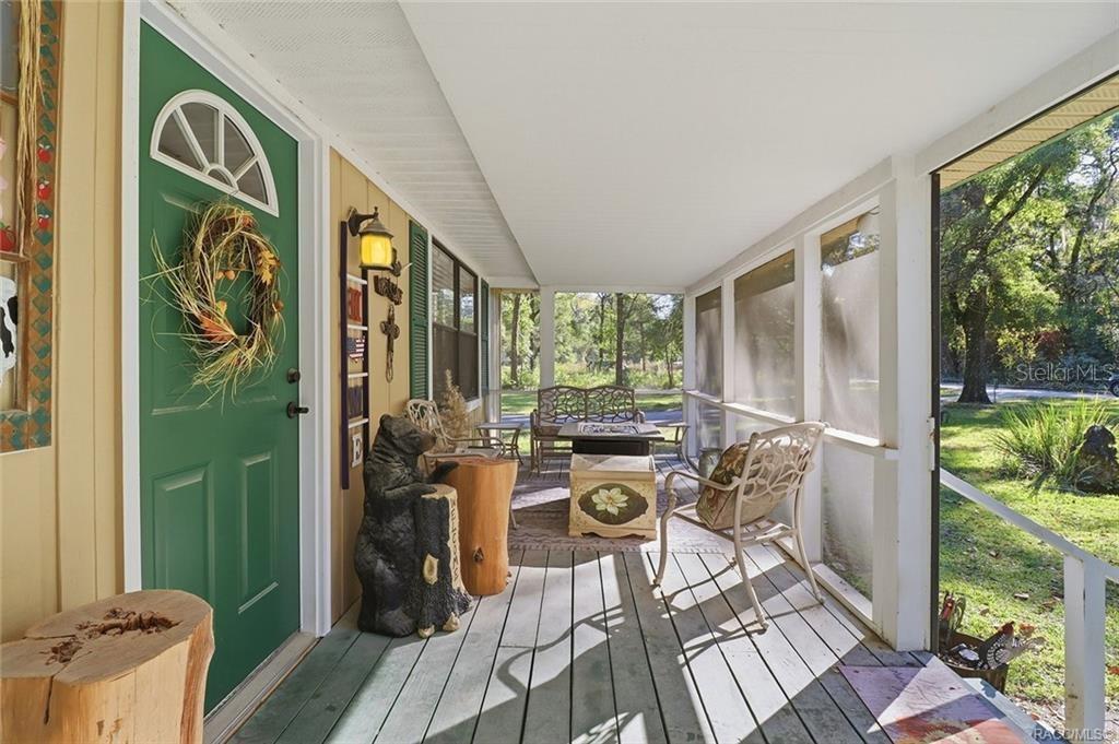 A screened-in porch features a green front door, wooden flooring, and outdoor seating — 8110 SW 88TH LANE, TRENTON, FL