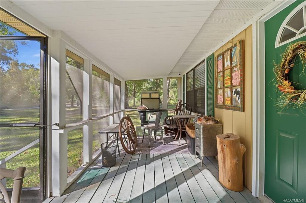 A screened-in porch with a green door, wooden flooring, and various rustic furniture pieces — 8110 SW 88TH LANE, TRENTON, FL