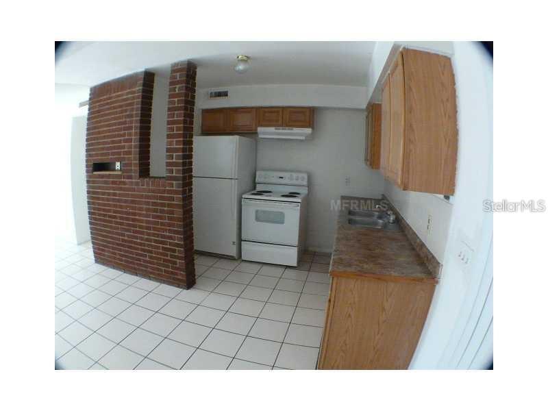 A kitchen features white appliances, wood cabinets, a brick accent wall, and white tile flooring — 895 PASADENA AVENUE, LONGWOOD, FL