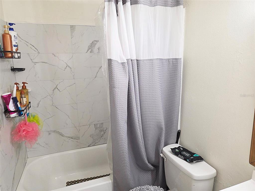 A bathroom features a white bathtub with marble-look tile walls and a grey shower curtain — 895 PASADENA AVENUE, LONGWOOD, FL