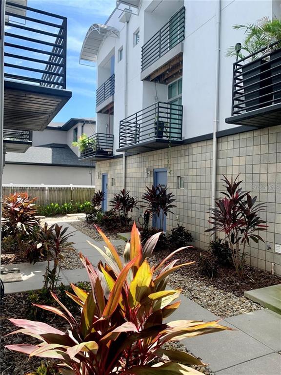 A multi-story building exterior features balconies with black railings and a landscaped walkway below — 5008 S MACDILL AVENUE UNIT 19, TAMPA, FL