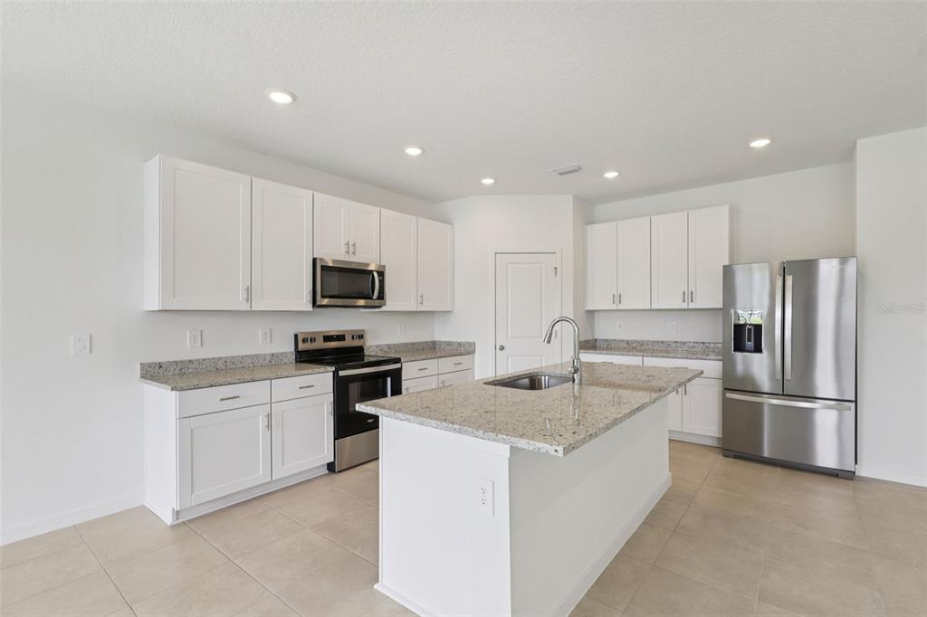 A kitchen features white cabinets, granite countertops, a center island, and stainless steel appliances — 73 WANDERING CREEK WAY, PALM COAST, FL