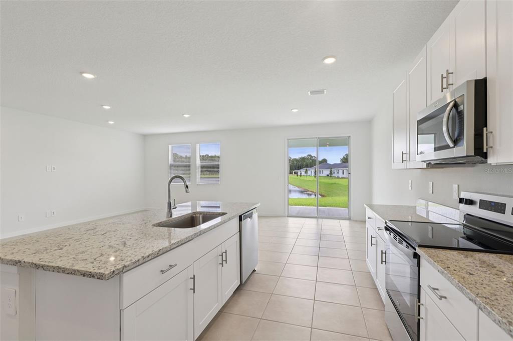 A kitchen with white cabinets, granite countertops, stainless steel appliances, and a sliding glass door — 73 WANDERING CREEK WAY, PALM COAST, FL