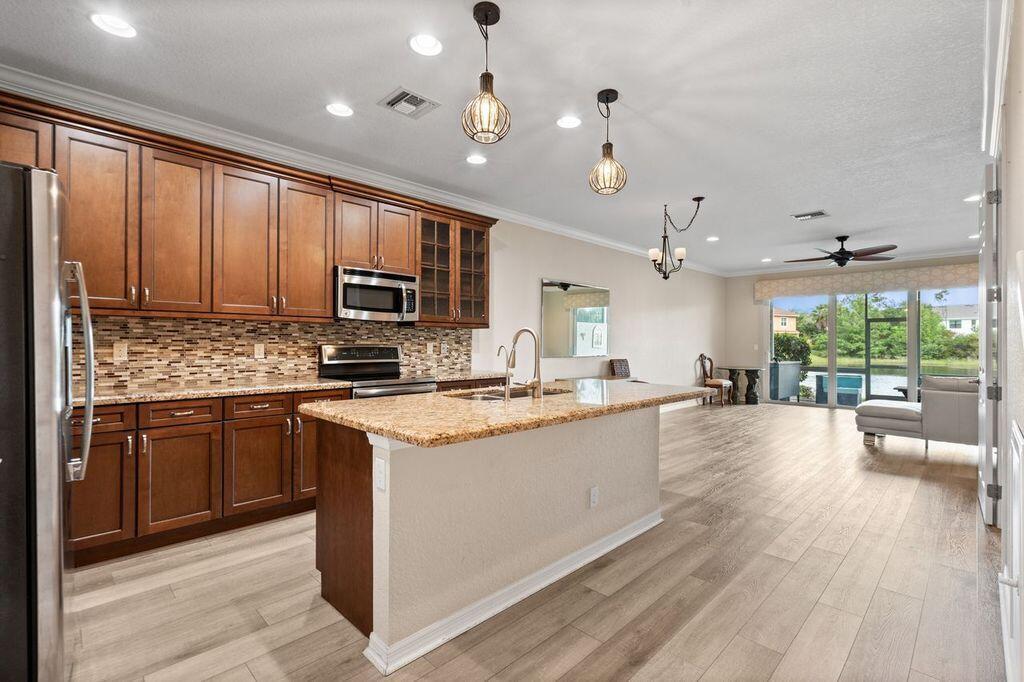 A kitchen with wood cabinets, granite countertops, and an island, opening to a living area — 626 SW Glen Crest Way, Stuart FL 34997, STUART, FL