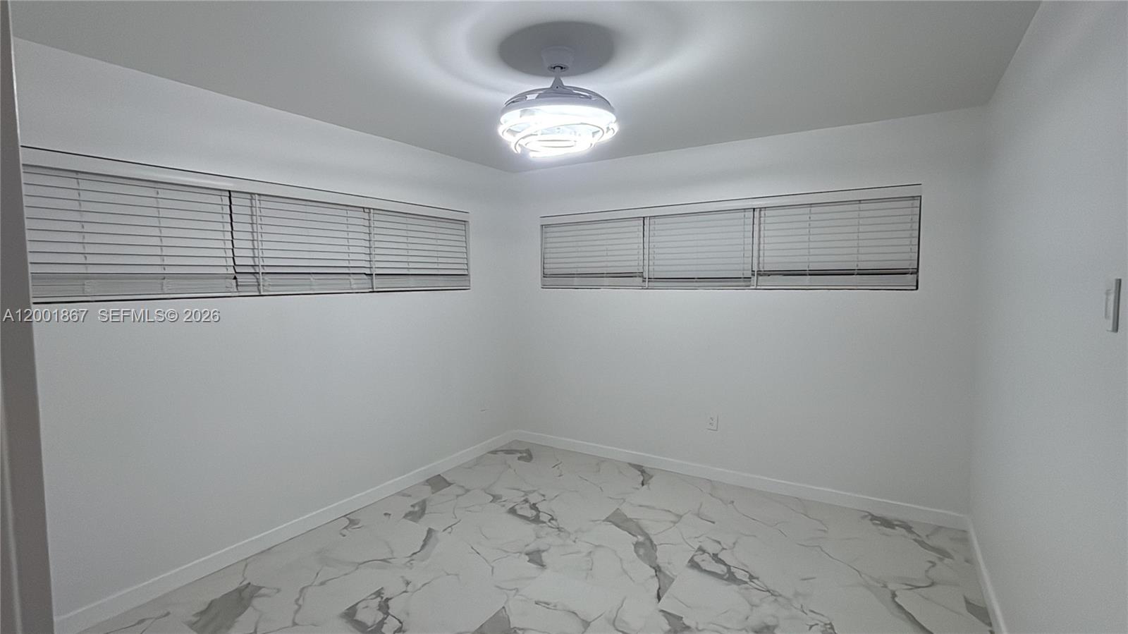 A bright, empty room features white walls, marble-patterned tile flooring, and a modern ceiling fan — 1629 Mayo St, Hollywood FL 33020, HOLLYWOOD, FL