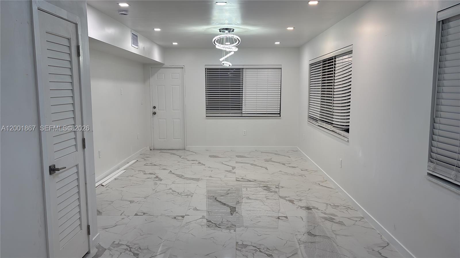 A bright room features white walls, marble-patterned tile floors, a modern chandelier, and window blinds — 1629 Mayo St, Hollywood FL 33020, HOLLYWOOD, FL