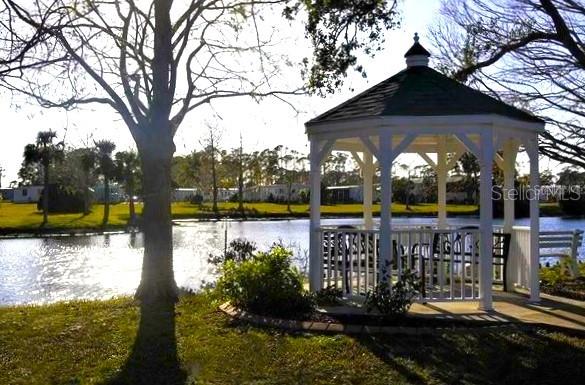A white gazebo sits on a grassy lawn beside a lake with trees in the background — 6418 KILOHEE COURT, NORTH PORT, FL