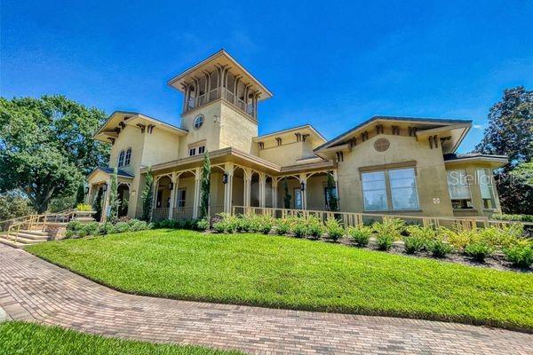A two-story tan house with a central tower and a brick walkway in the foreground — 102 VISTA VERDI CIRCLE UNIT 100, LAKE MARY, FL