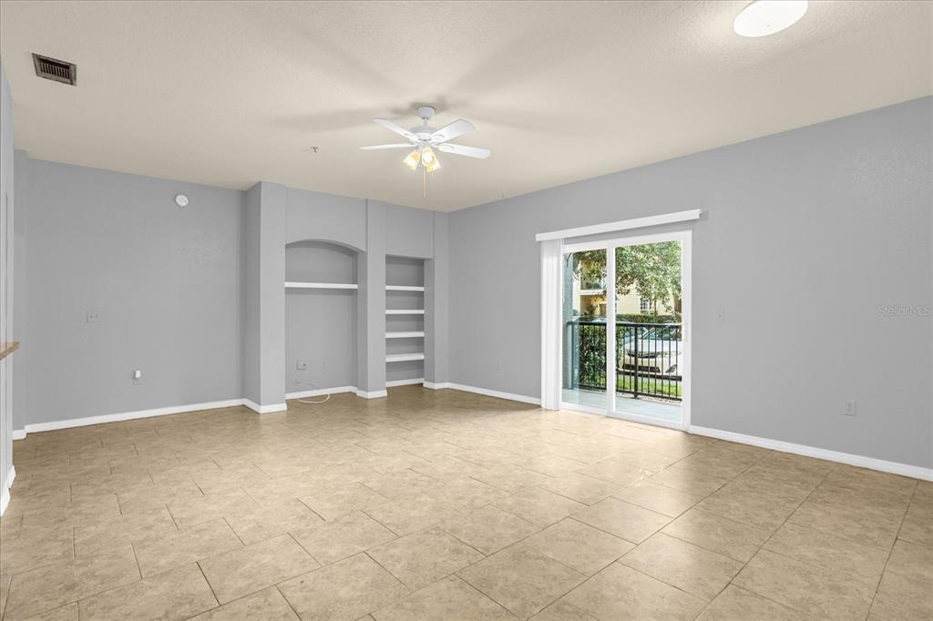 A living room with light gray walls, tile flooring, a ceiling fan, and built-in shelving — 102 VISTA VERDI CIRCLE UNIT 100, LAKE MARY, FL