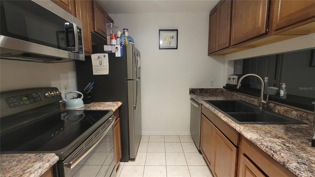 A galley kitchen features wood cabinets, stainless steel appliances, and dark countertops — 4000 SW 23RD STREET UNIT 6-303, GAINESVILLE, FL