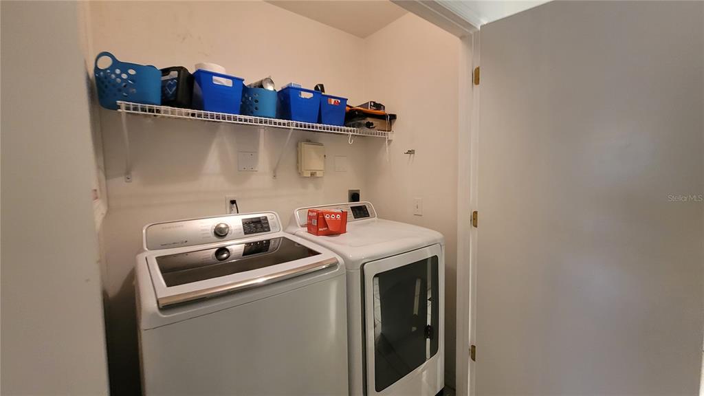 A laundry room features a white washer and dryer beneath a wire storage shelf — 4000 SW 23RD STREET UNIT 6-303, GAINESVILLE, FL