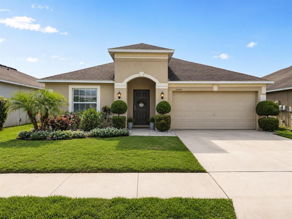 A single-story beige house with a two-car garage and a landscaped front yard — 15406 FEATHER STAR PLACE, RUSKIN, FL
