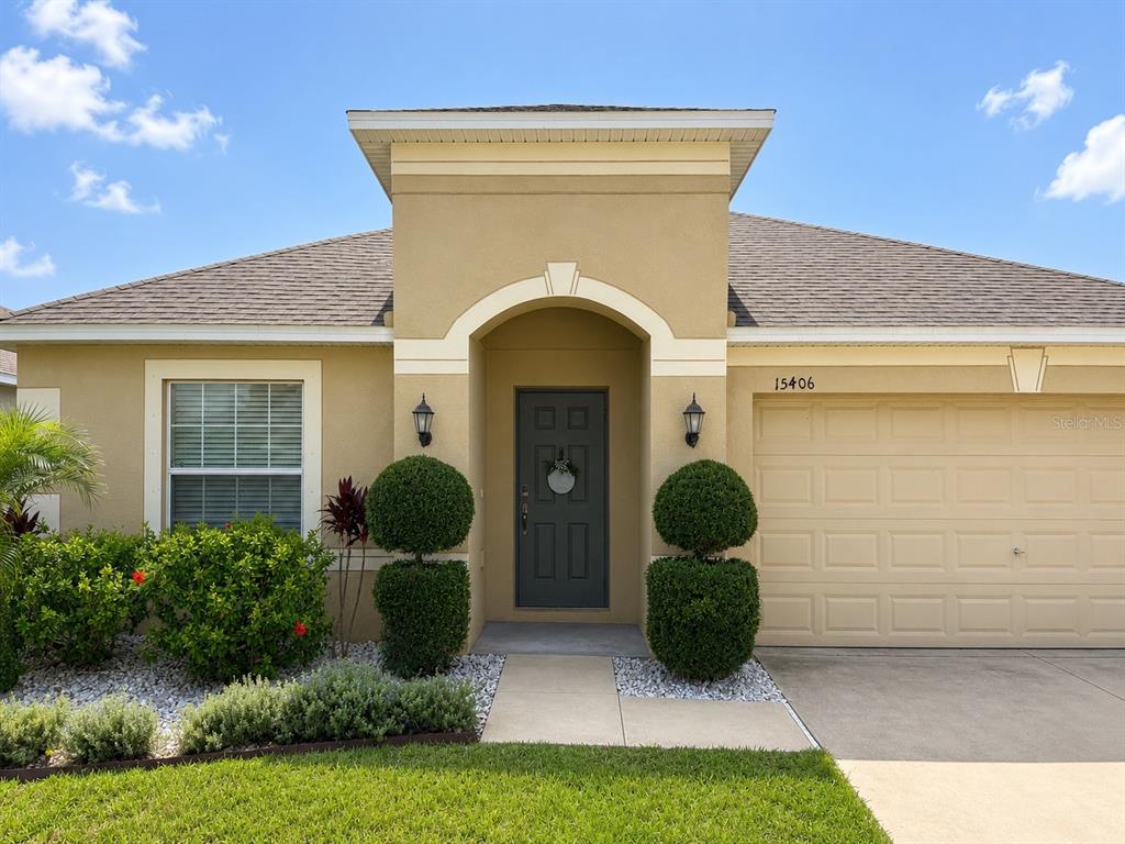 The exterior of a tan stucco house features a dark front door and a garage — 15406 FEATHER STAR PLACE, RUSKIN, FL