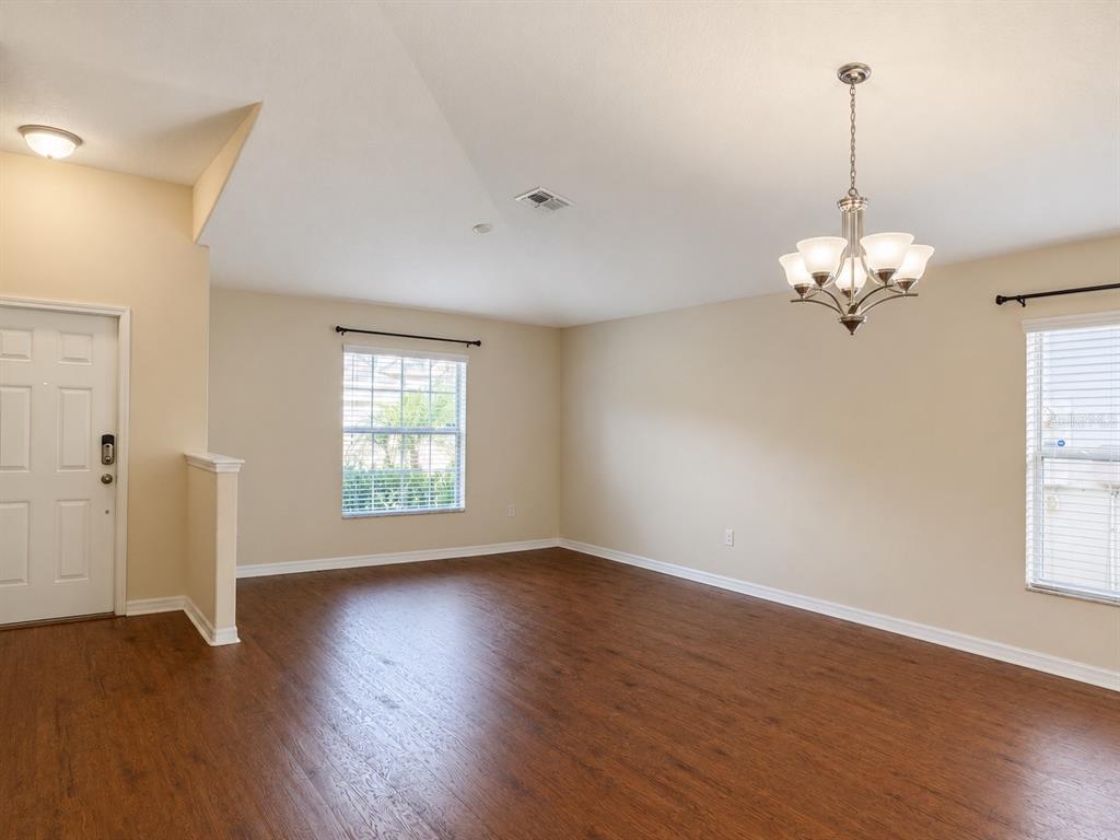 An empty living room features wood-look flooring, beige walls, a chandelier, and two windows — 15406 FEATHER STAR PLACE, RUSKIN, FL