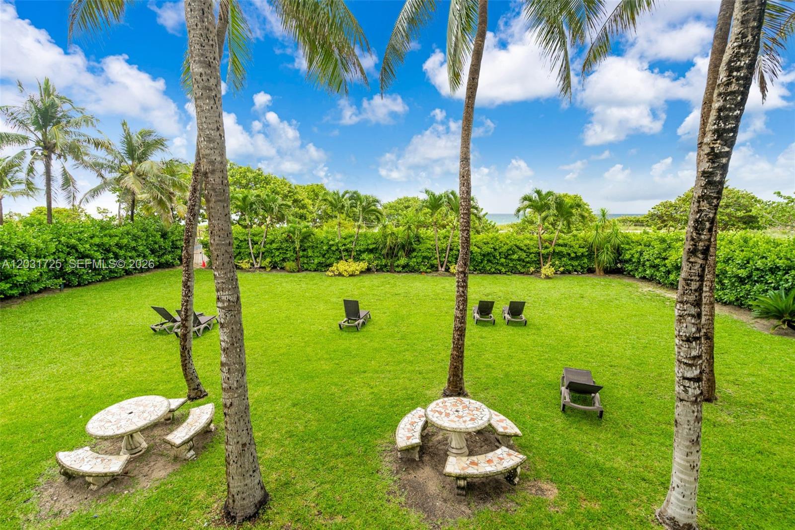 A grassy backyard features palm trees, stone picnic tables, and lounge chairs near the ocean — 9195 Collins Ave # 601, Surfside FL 33154, SURFSIDE, FL