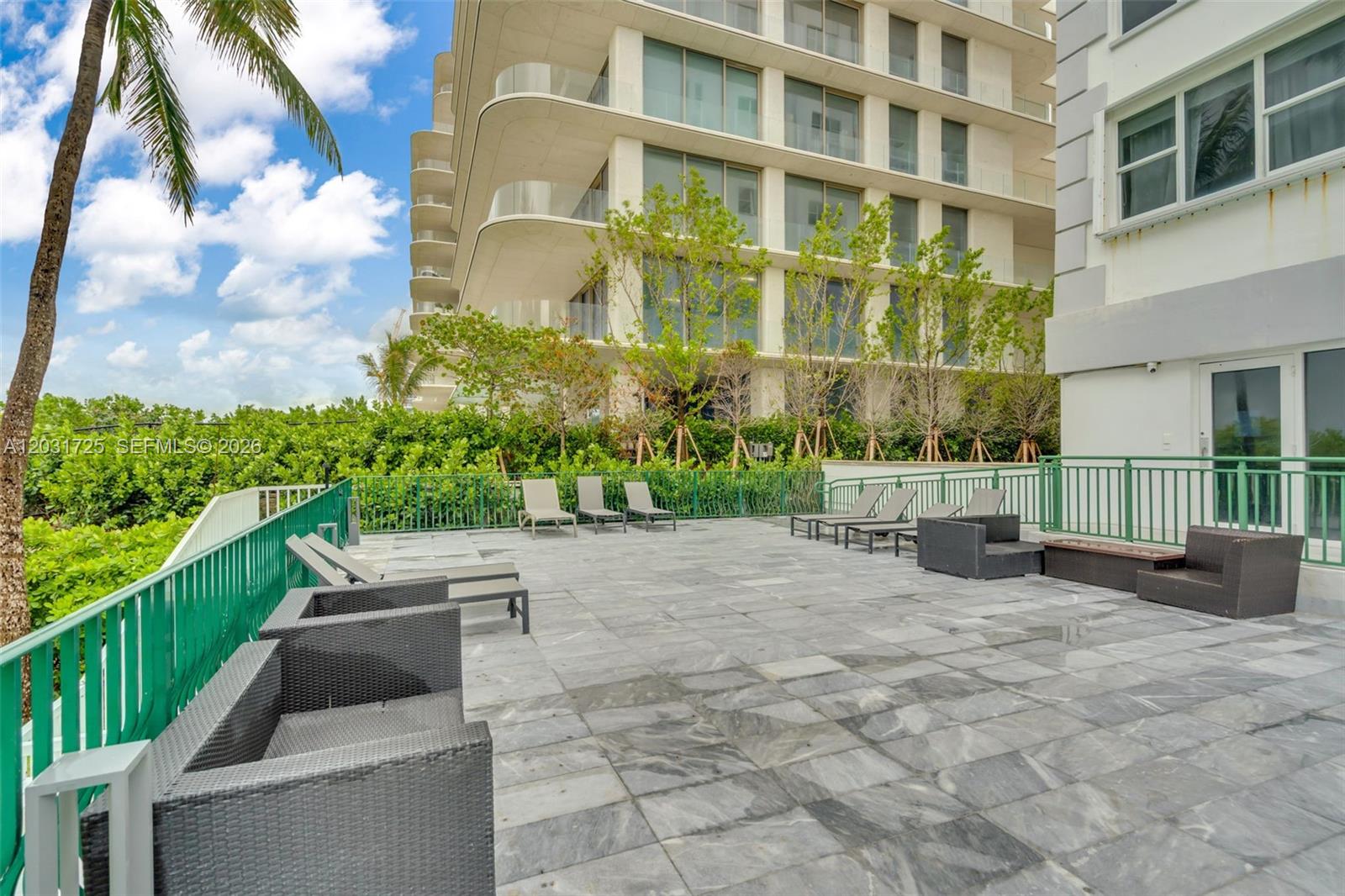 A stone-paved outdoor terrace features lounge chairs and wicker furniture enclosed by a green railing — 9195 Collins Ave # 601, Surfside FL 33154, SURFSIDE, FL