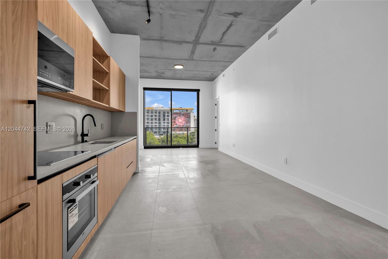 A modern kitchen with wood cabinets and concrete ceilings opens to a balcony with views — 91 NW 27th St # 201, Miami FL 33127, MIAMI, FL