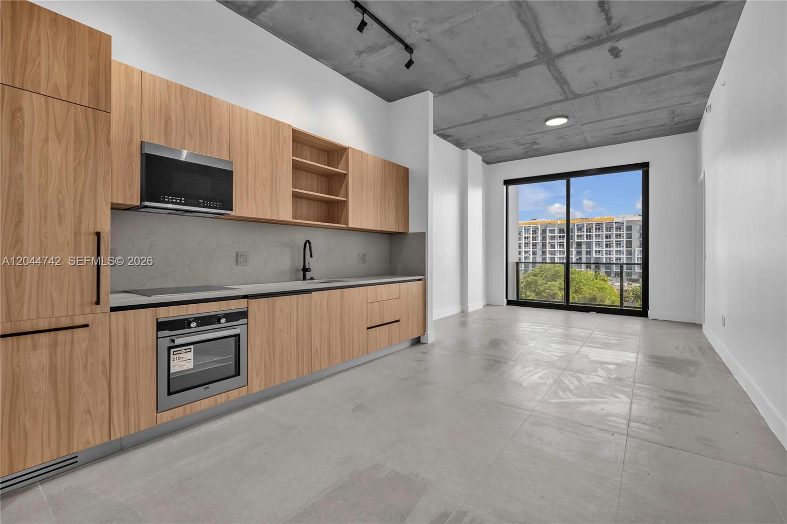 A modern kitchen features light wood cabinetry, concrete ceilings, and a large sliding glass door — 91 NW 27th St # 201, Miami FL 33127, MIAMI, FL