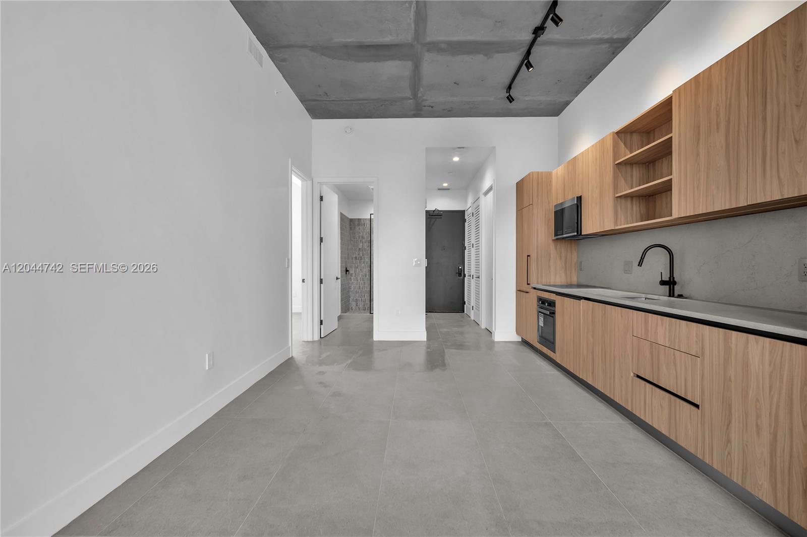 A modern kitchen features light wood cabinetry, gray tile flooring, and an exposed concrete ceiling — 91 NW 27th St # 201, Miami FL 33127, MIAMI, FL
