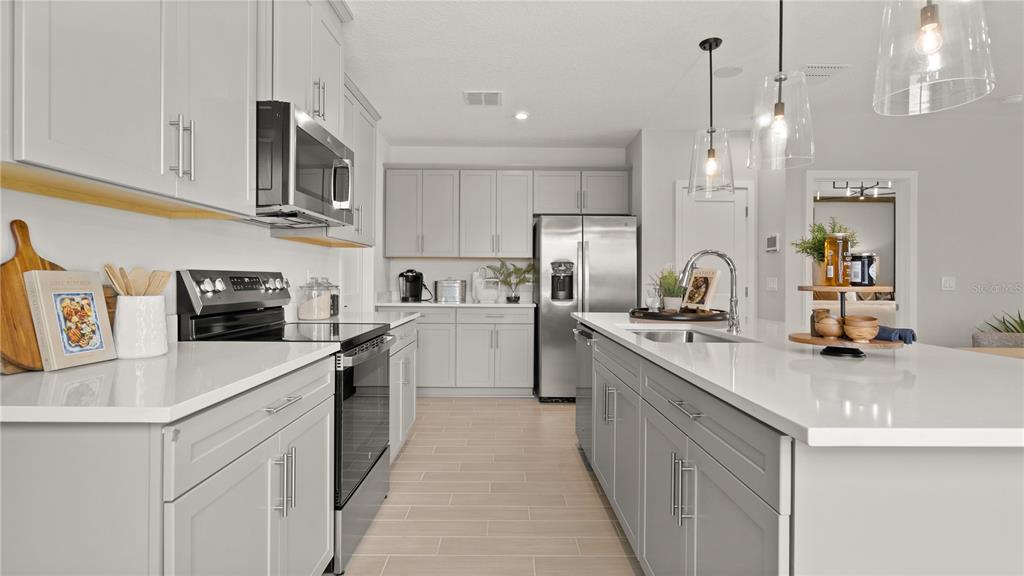 A modern kitchen features light gray cabinets, stainless steel appliances, and a white quartz island — 416 LIBERTY BEND, HAINES CITY, FL