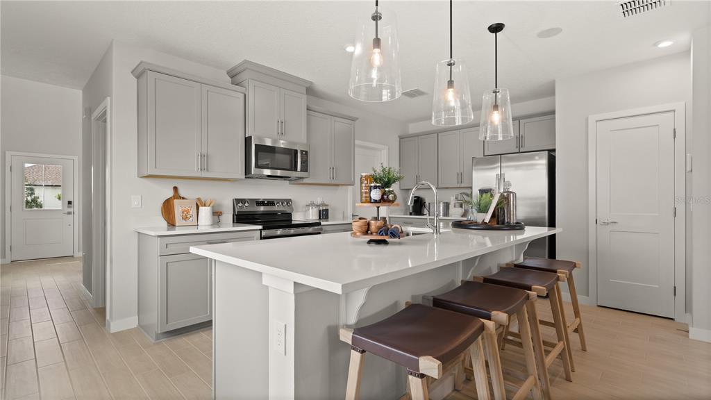 A modern kitchen features gray cabinetry, a white quartz island, and three wooden bar stools — 416 LIBERTY BEND, HAINES CITY, FL