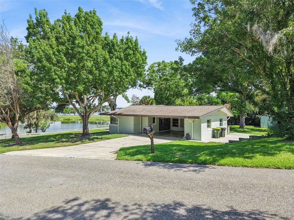 A single-story house with a carport and driveway sits on a grassy lot near water — 290 CARROLL STREET, CLERMONT, FL
