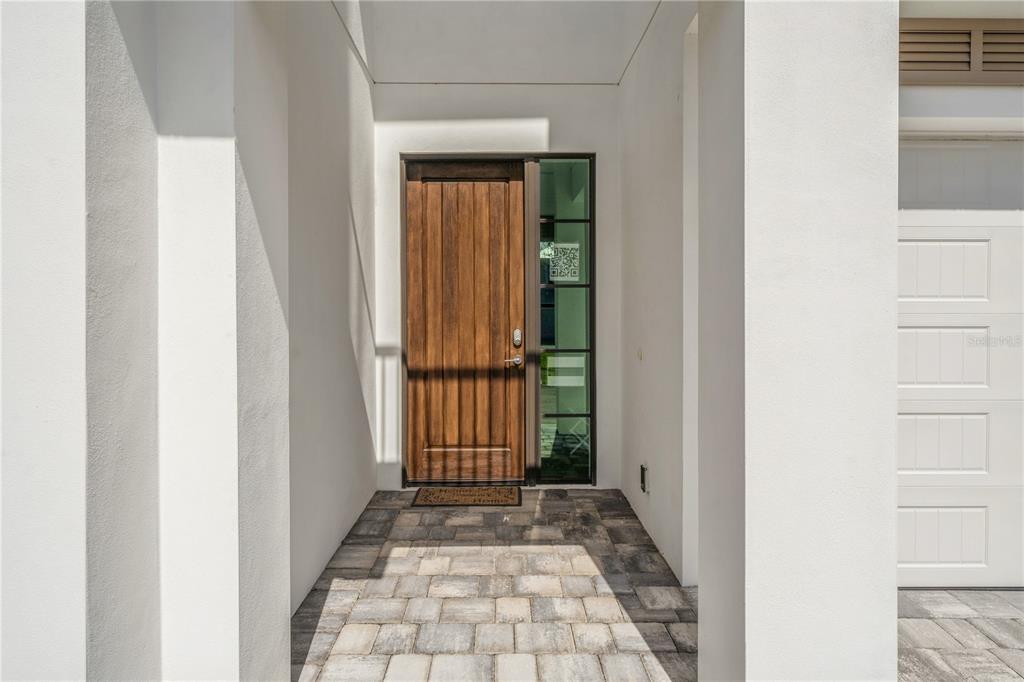 A wooden front door with a side window sits under a covered entryway with pavers — 132 OCEAN ESTATES DRIVE, HUTCHINSON ISLAND, FL