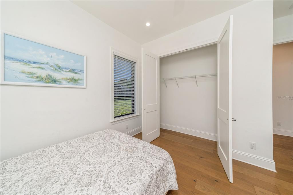 A bedroom with white walls, wood flooring, a bed, a window, and an open closet — 132 OCEAN ESTATES DRIVE, HUTCHINSON ISLAND, FL